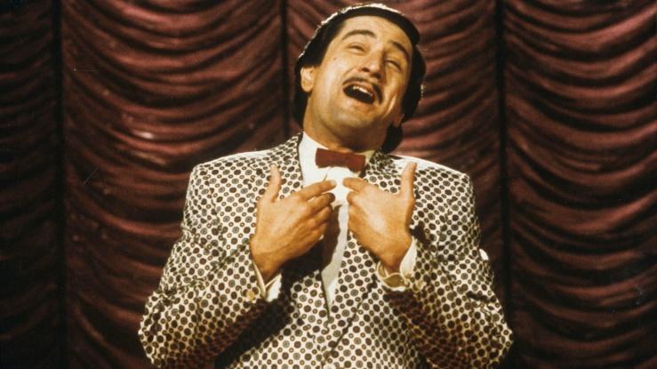 A screen still from the film The King of Comedy, featuring Robert De Niro as Rupert Pupkin, standing on a stage and doing his stand up set.