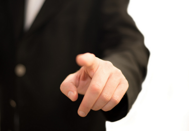 A close-up view of a finger being pointed at the camera. The person pointing appears to be wearing a suit. 