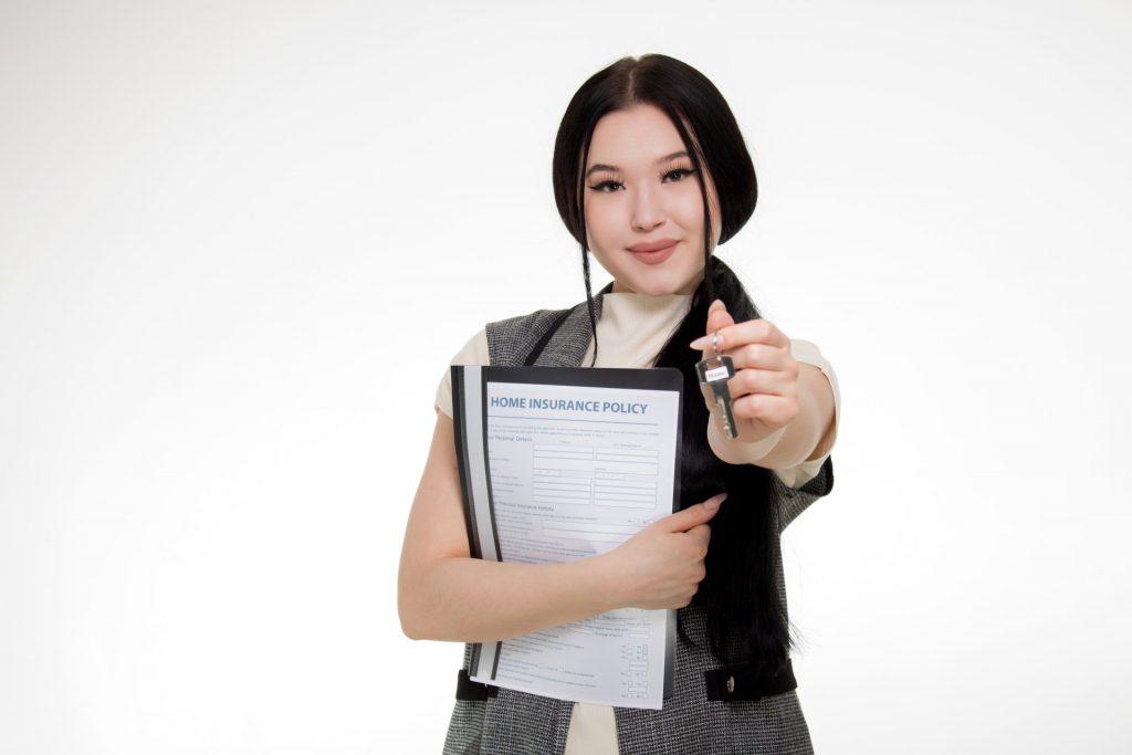 A woman holding some papers for home insurance and a key up towards the camera.