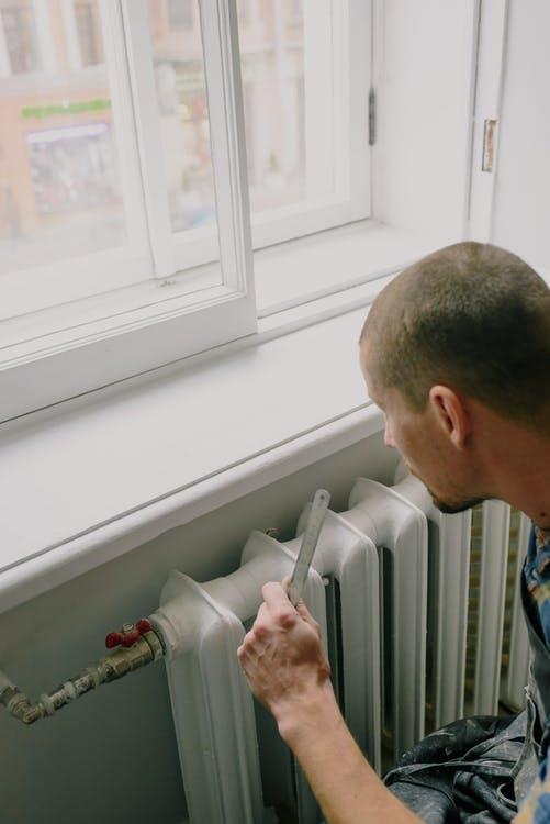 From above side view of crop anonymous male worker with ruler near radiator and windowsill in house