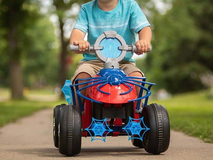 toddler riding a spiderman electric tricycle on a sidewalk