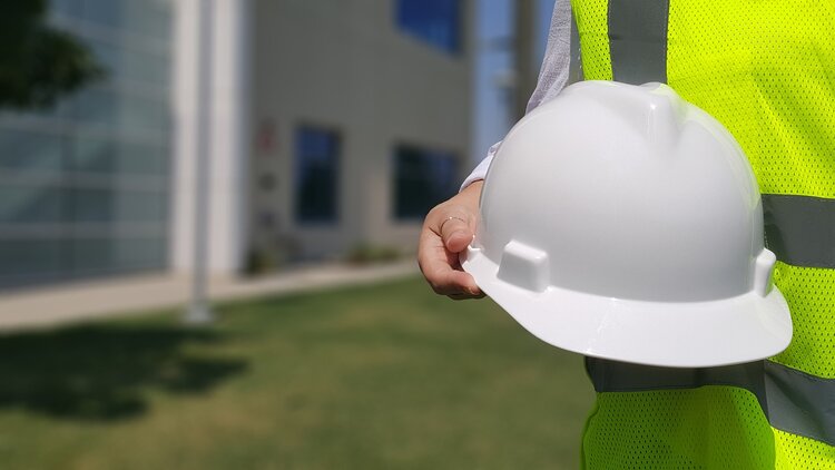 Construction workers in a reflective vest holding white hard hat.