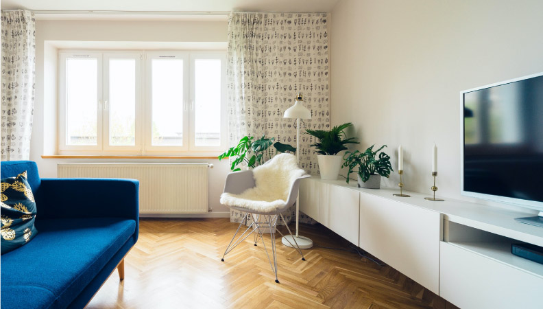 Interior view of an apartment living room. The couch is low and the curtains are hung high above the windows to create the appearance of more space in the room.