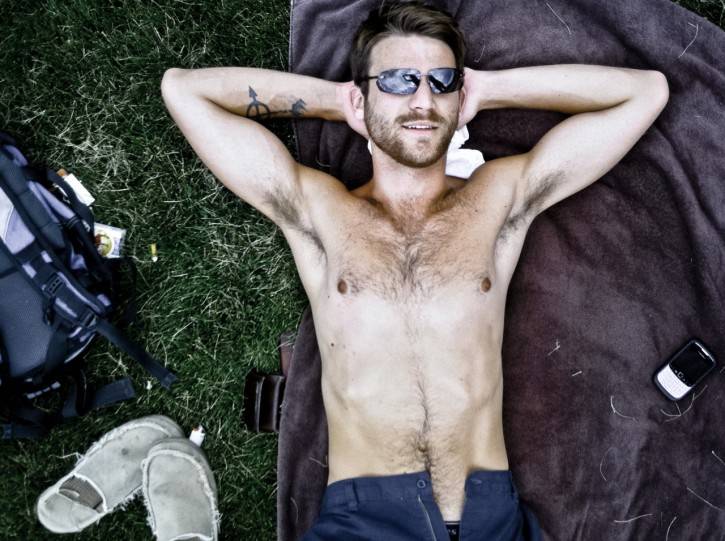 gay male lying down on a picnic blanket wearing shades shirtless while using his hands to support his head