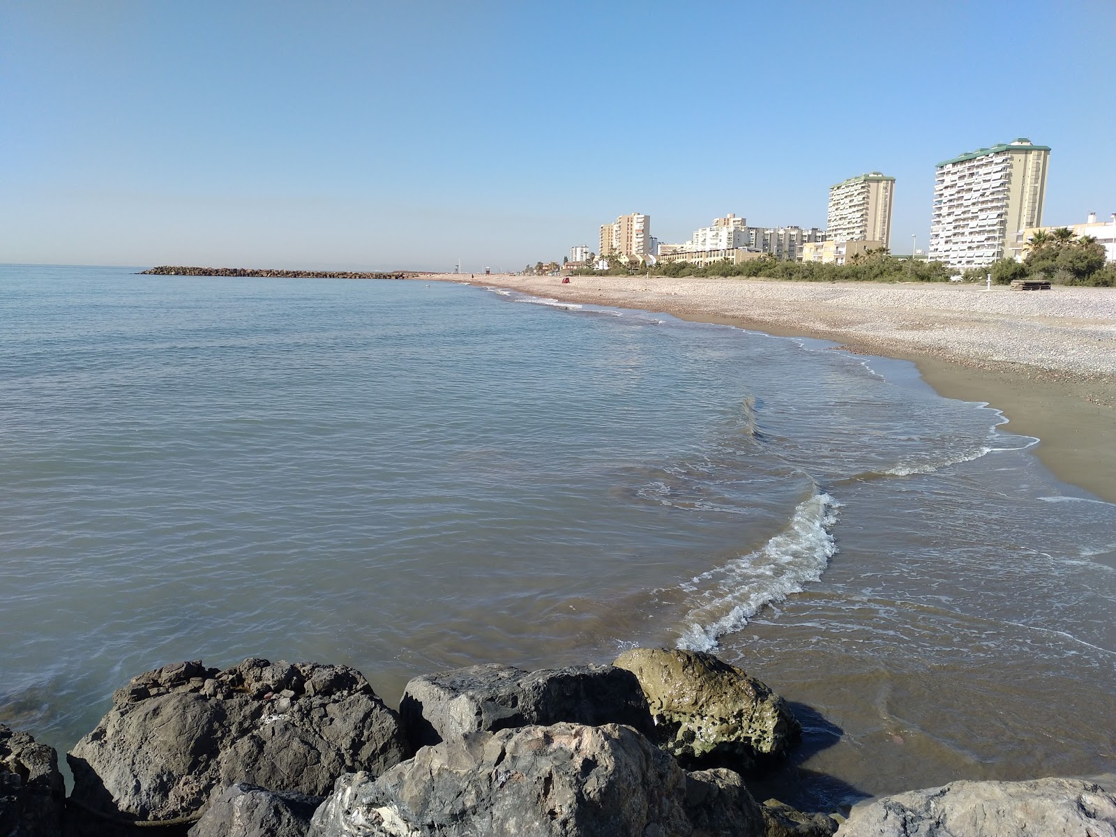 Foto av Stranden Puig med musta hiekka ja kivi yta