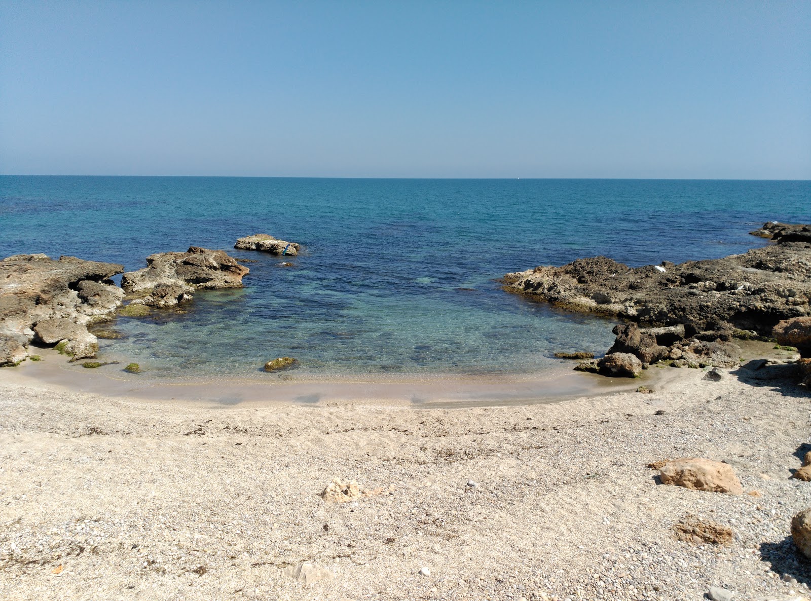 Foto av Cala del Moro med musta hiekka ja kivi yta