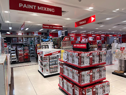 Image of a hardware store interior featuring aisles with shelves stocked with tools, tapes, adhesives, and fans. Prominent signage shows sections for "Paint Mixing," "Tools," and "Ace Exclusives." The floor is tiled, and the lighting is bright. Products are neatly organized on shelves and displays.