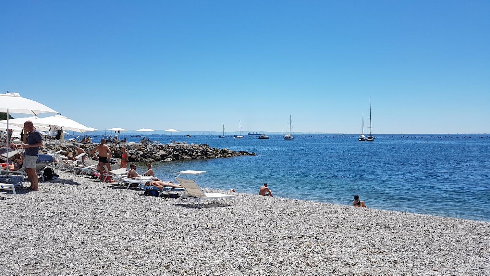Foto af Spiaggia di Portopiccolo Sistiana bakket op af klipperne