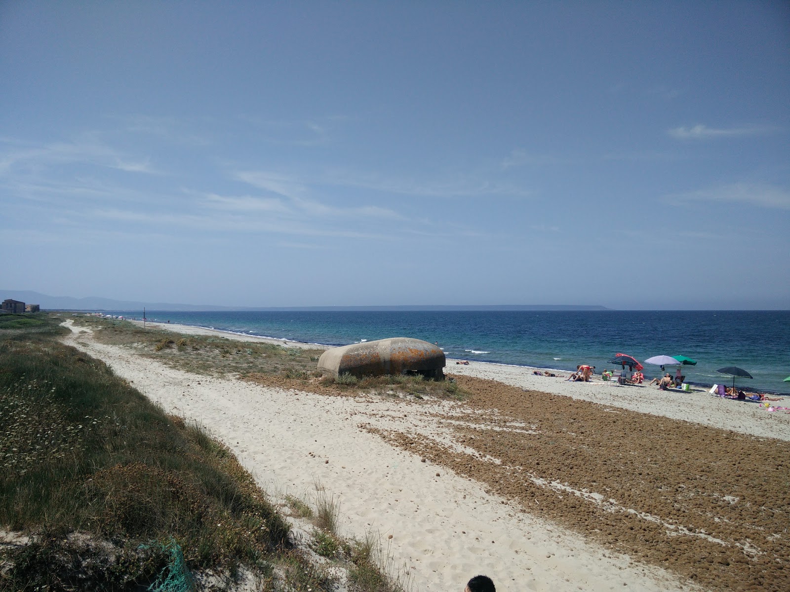 Primo piano di Arborea Beach II con coste sabbiose dorate e acque blu limpide, con un sfondo di alberi e vegetazione verde.