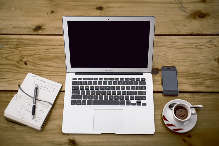 A macbook sitting on a table next a coffee and a notepad to show how how a remote job is