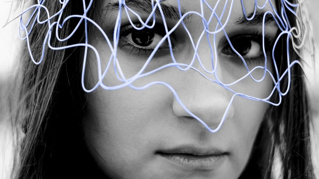 black and white photo portrait of female presenting person with color pop blue wires layered over their eyes