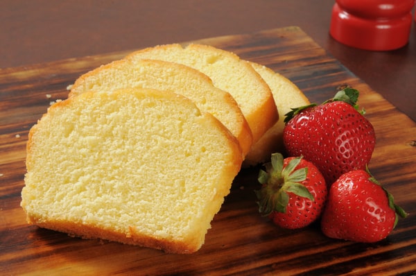 Slices of pound cake with three strawberries on the side, served on a wooden board