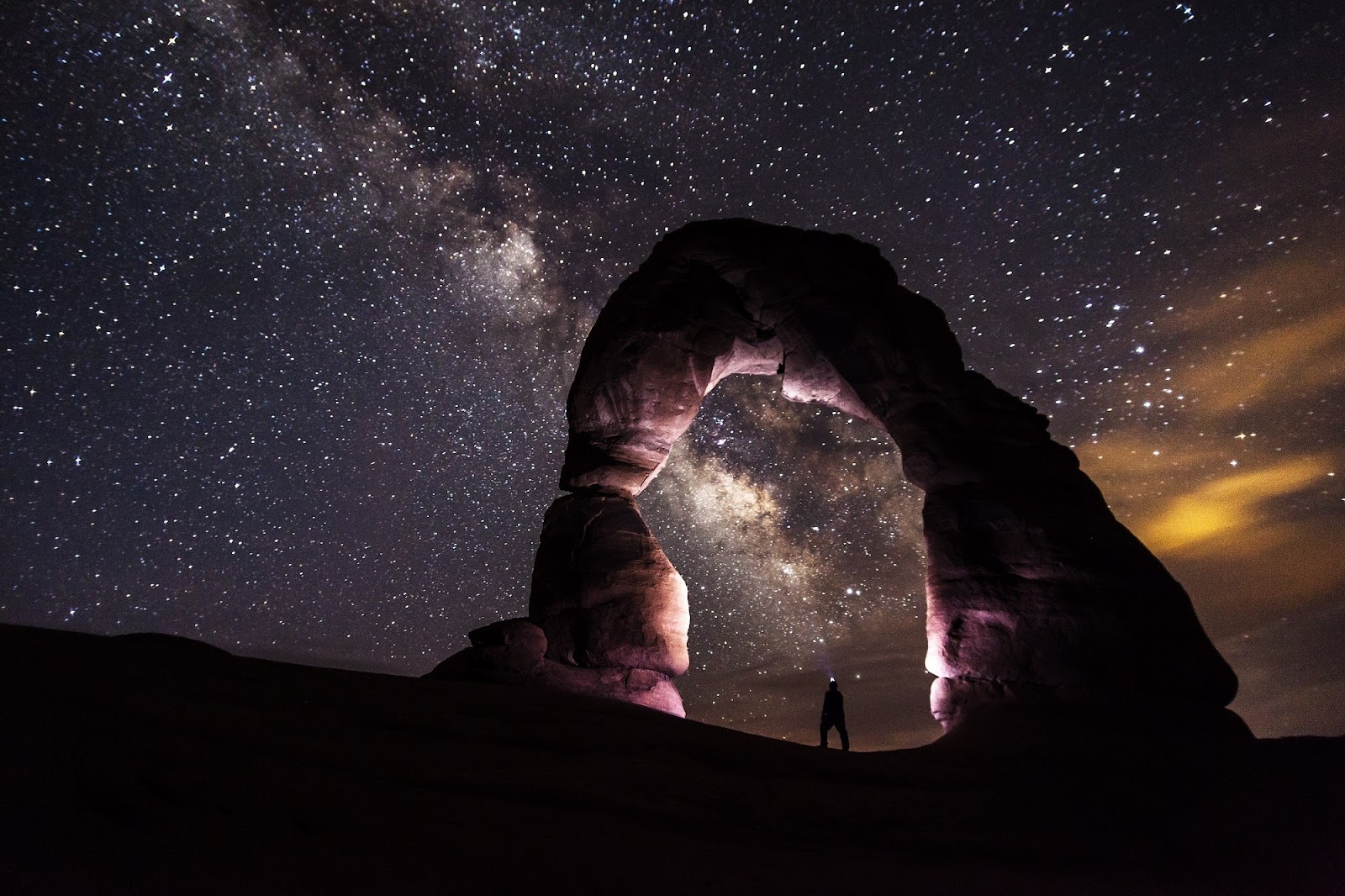 Person standing under Delicate Arch at nighttime
