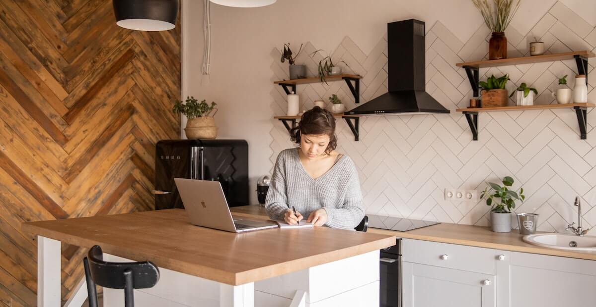 Woman sitting at desk, taking notes in front of laptop