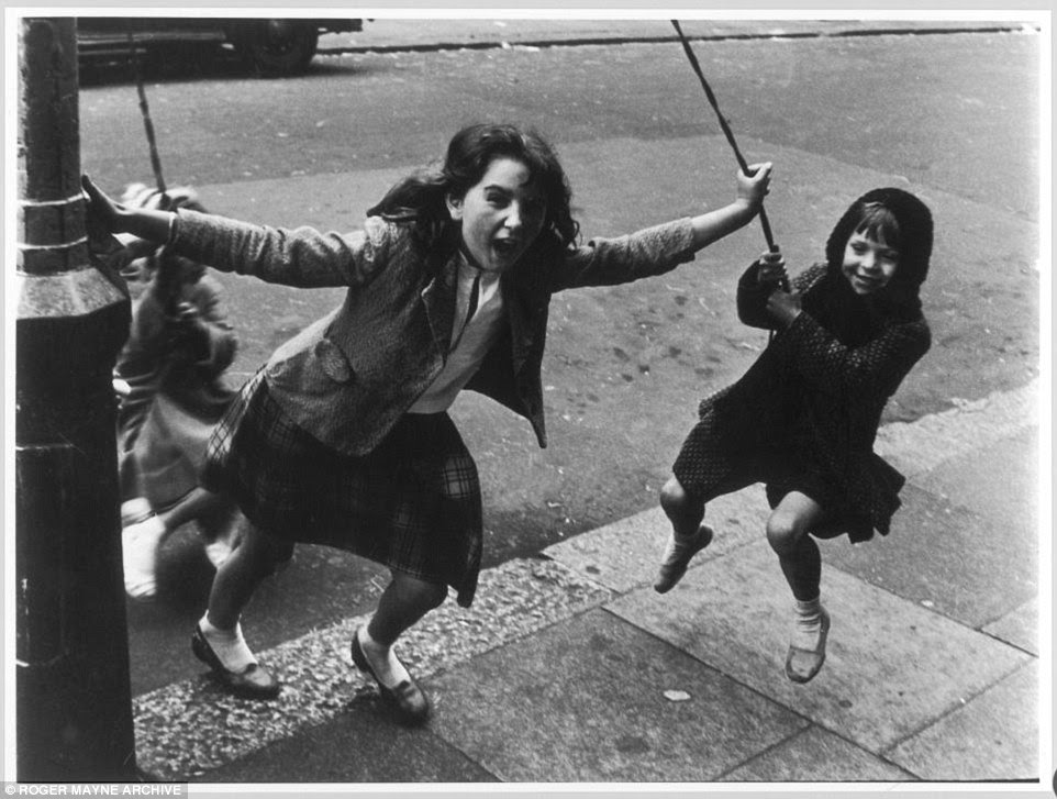 Two girls swing from ropes of a lamppost in Kensingston's Southam Street in 1958