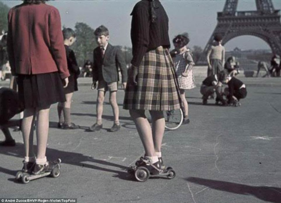 Too young to understand: Girls and boys play in what appear to be the early forerunners of rollerskates against the backdrop of the Eiffel Tower on central Paris's Champ de Mars
