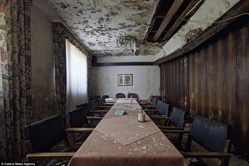 PIC BY DANIEL BARTER / CATERS NEWS - (PICTURED: Main dining table - Burnt out hotel) - Even the powerhouse of Europe has its fair share of abandoned properties and empty shop fronts as seen in these captivating pictures of decaying buildings Germany. Photographer Daniel Barter, 30, from London travelled Berlin and the surrounding countryside to capture buildings in need of work on film. Far from being resplendent in vintage glory, the deserted music venues and crumbling hospitals are a shadow of their former selves. German eagle motifs flake off ceilings and concert halls designed for hundreds have not seen a show for years. SEE CATERS COPY.