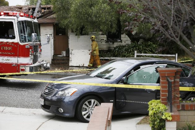 A firefighter walks past a car with bullet holes across a home that caught fire in Santa Monica, Calif. Friday, June 7, 2013. Two people were found dead Friday in a burned home near the school, where someone sprayed a street corner with gunfire, wounding at least three people, authorities said. (AP Photo/Damian Dovarganes)