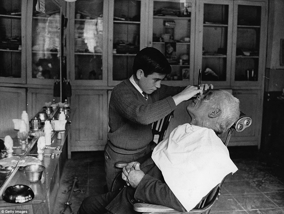 Timeless tradition: A young barber learns the tricks of the trade while at work on an elderly client in Italy