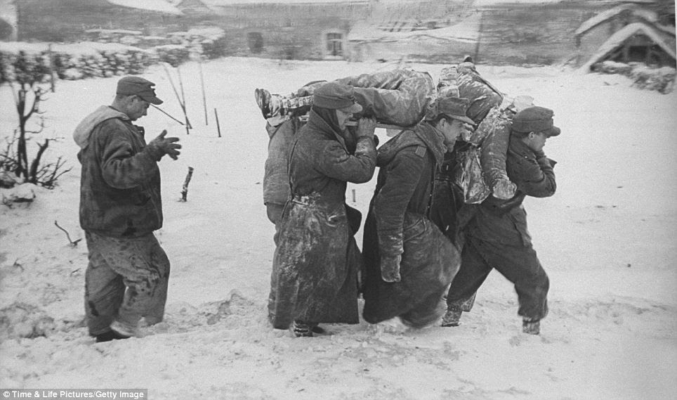 German POWs carrying body of American soldier killed in Battle of Bulge through snowy Ardennes field
