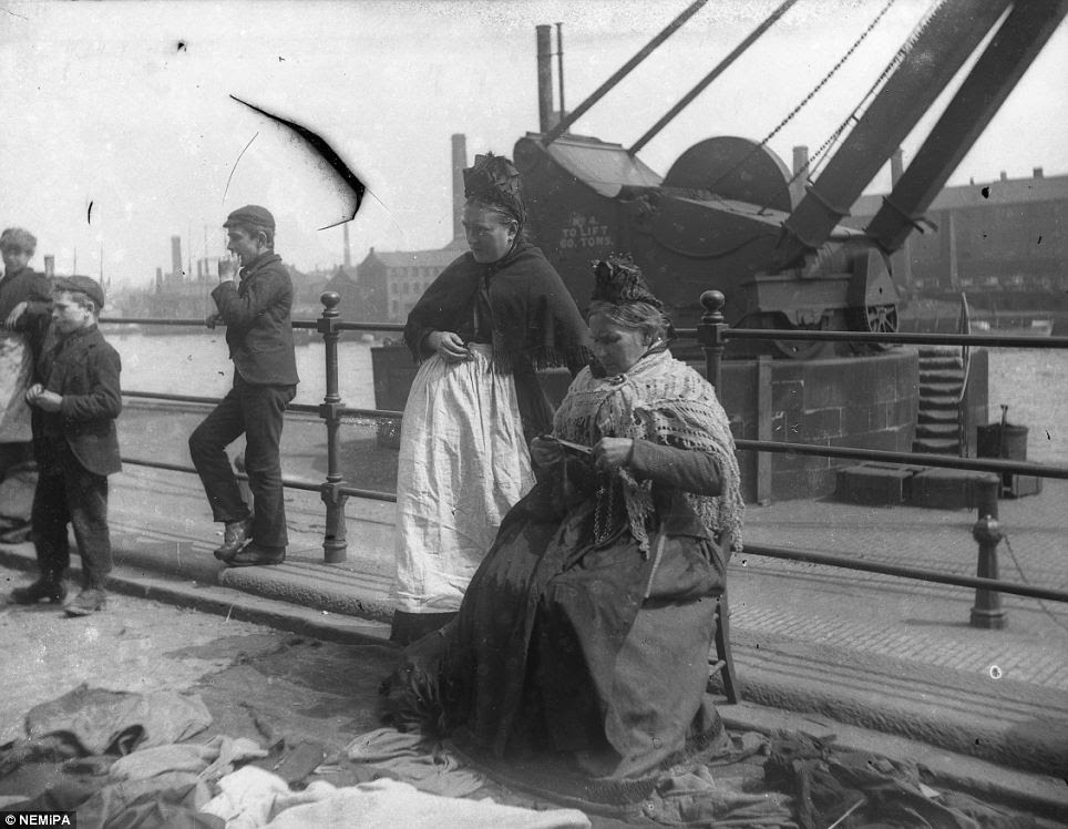 Women's work: Two Newcastle matrons pass the time over some knitting by the city's Quayside, while children loiter nearby