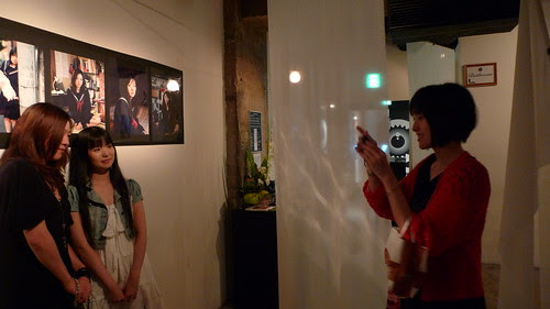 Photo of photographer Kawori Inbe taking photos of her two models in front of the photos they modelled for