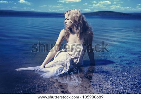 Young sexy blond woman in the blue water in wet white dress