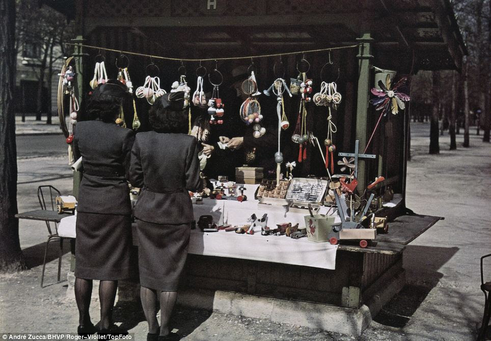 Trinkets: Two women in military-style uniforms shop at a stall selling toys. Zucca's pictures show both the hardship for French civilians and the collaborations between the Vichy regime and the Nazis