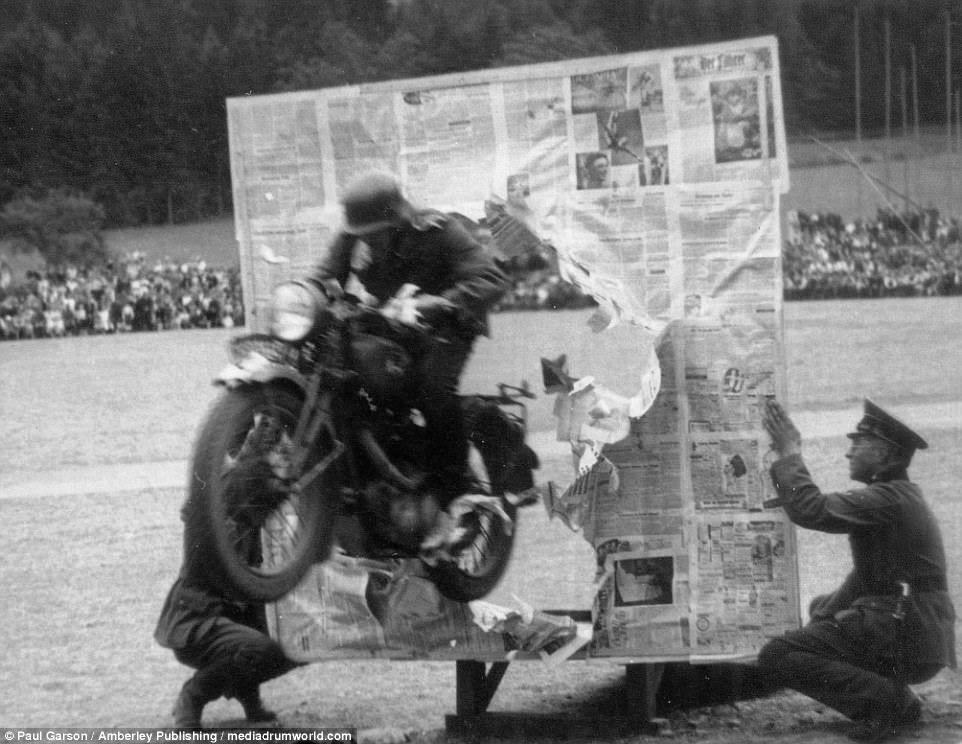 A German motorcyclist jumps through a sheet of newspaper before crowds in a display before the war started in June 1938