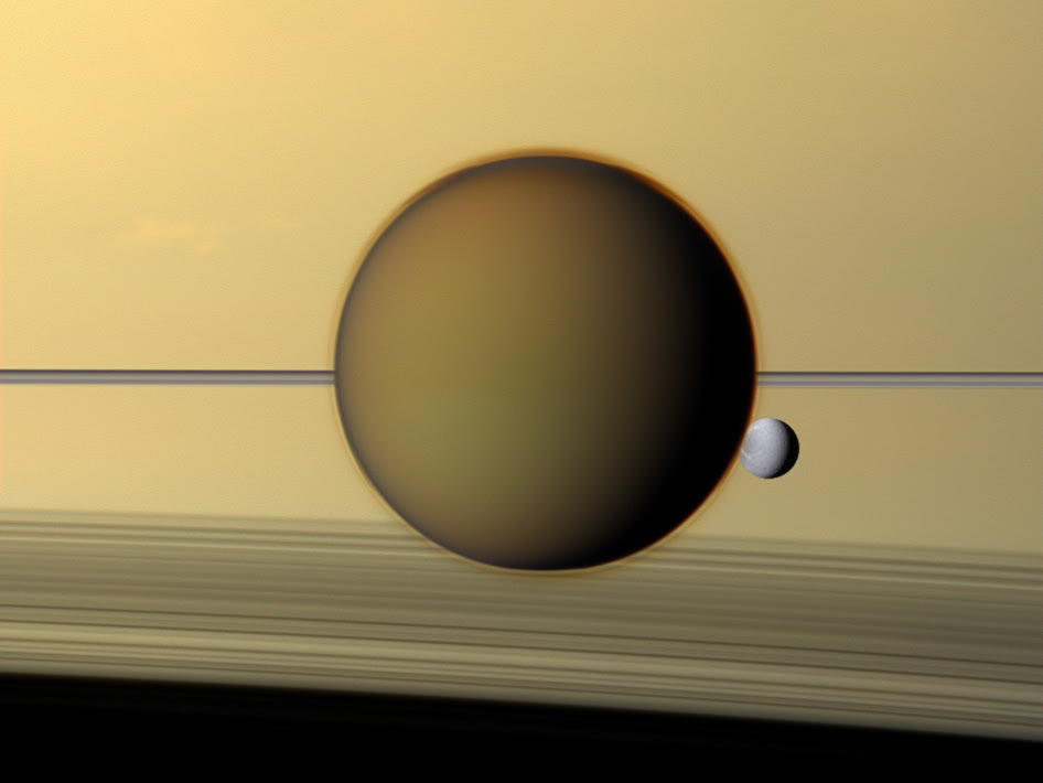 As nuvens de Titã não entregam nada; veja Saturno ao fundo. A lua cinzenta menor é Dione.