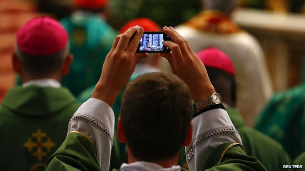 A priest takes a picture as Pope Francis celebrates a Mass to mark the opening of the synod on the family in Saint Peter's Square at the Vatican October 5 2014