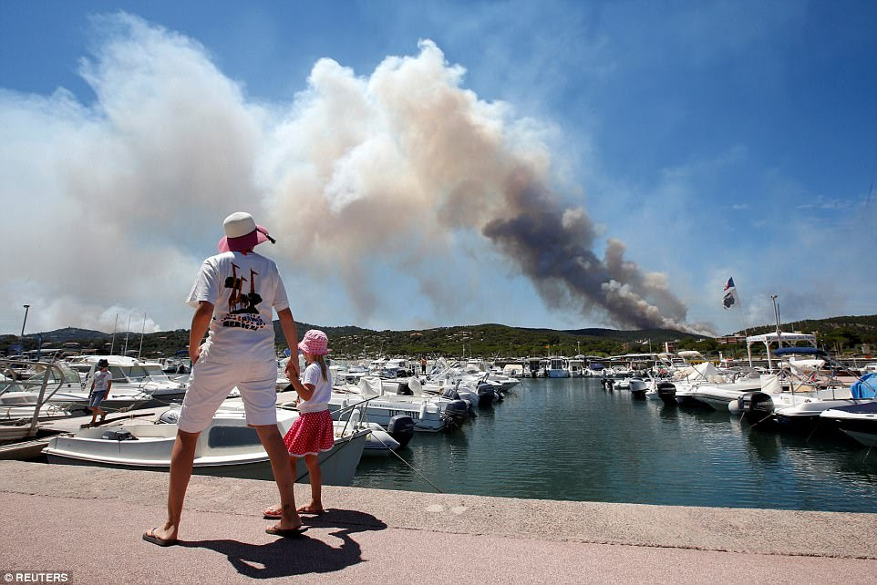 A woman and her daughter look at a plume of smoke from burning fires that fills the sky in the popular resort in the South of France