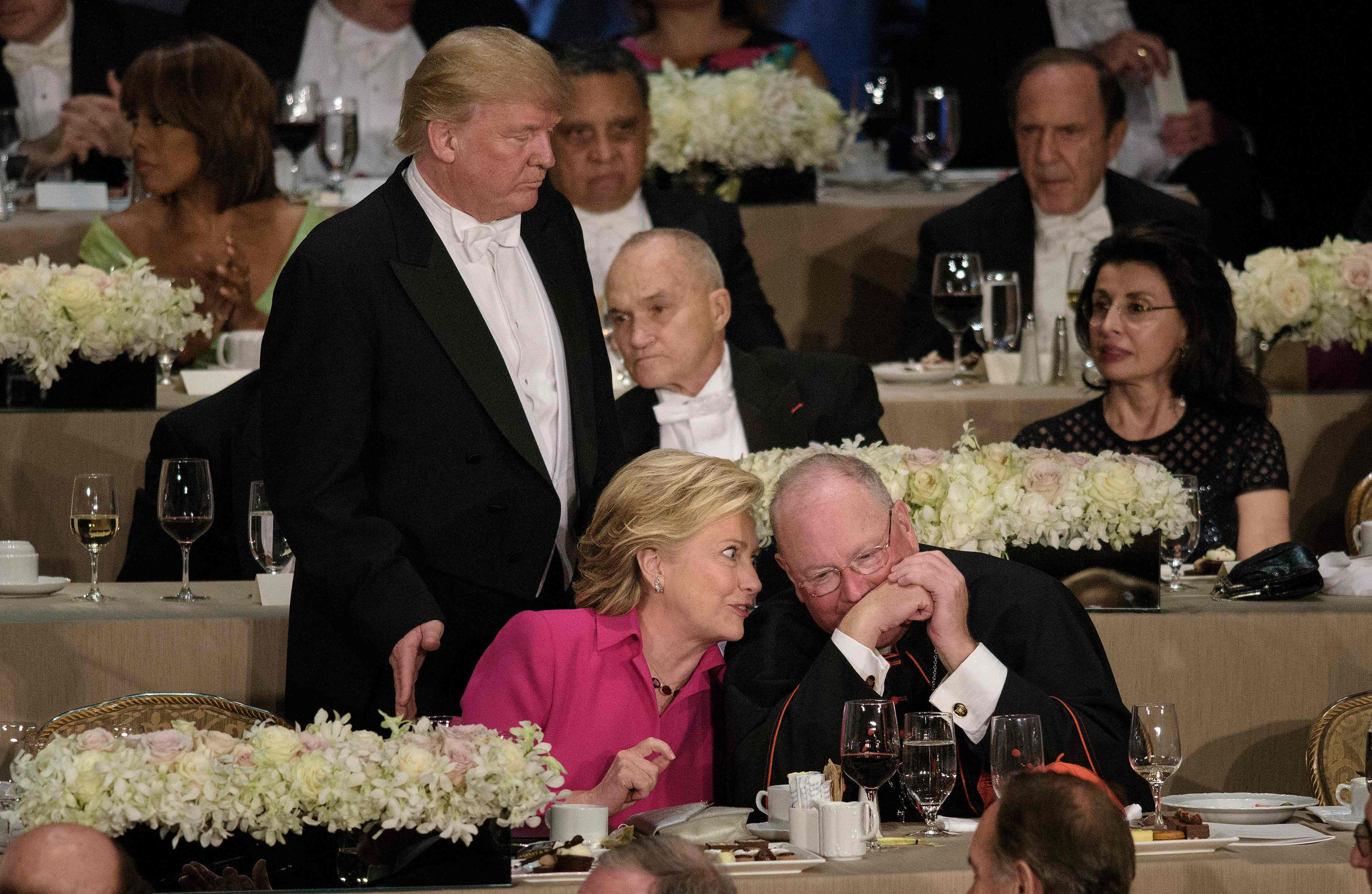 Republican presidential nominee Donald Trump pats Democratic presidential nominee Hillary Clinton on the back as she speaks with Timothy Cardinal Dolan, Archbishop of New York, during the Alfred E. Smith Memorial Foundation Dinner at Waldorf Astoria October 20, 2016 in New York, New York. / AFP PHOTO / Brendan Smialowsk