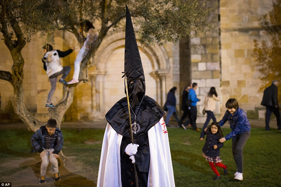 Everyday event: Children play in the background as a penitent watches a march from 'Jesus en su Tercera Caida' brotherhood during a procession in Zamora, Spain