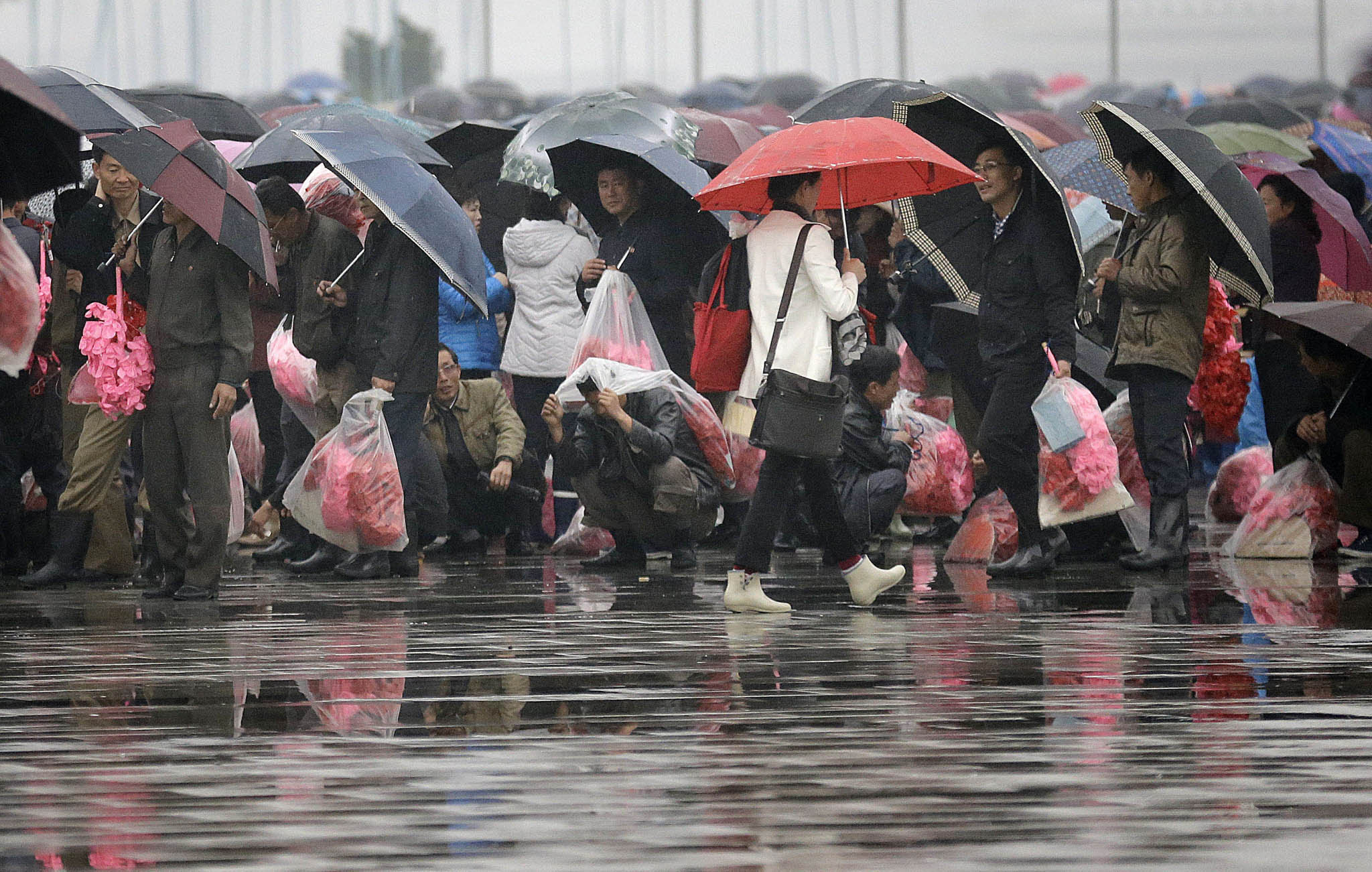 North Korean men and women carry bouquets of decorative flowers as they wait at the Kim Il Sung Square