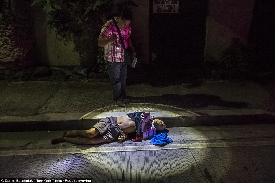 An unidentified body that was found with his head wrapped in packing tape, his hands tied behind his back and a cardboard sign that read, "A pusher who won't stop will have his life ended," on a street in Manila, Philippines