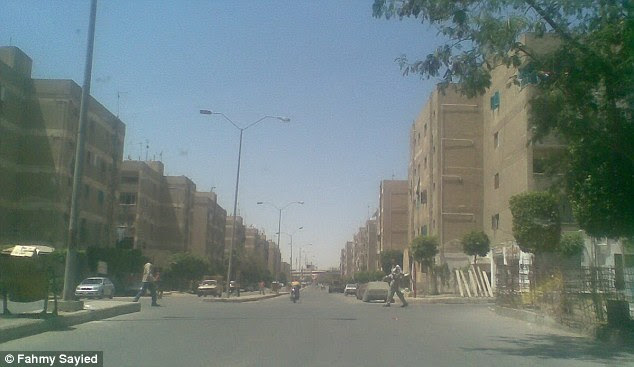 The two figures appear to tower over cars driving through the streets of the small Egyptian town