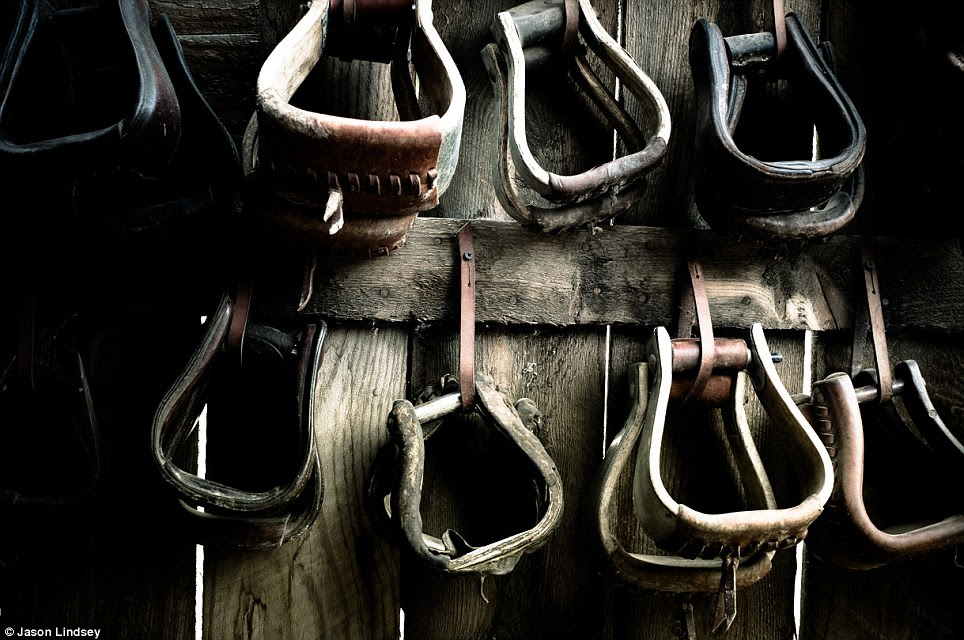 Rows of stirrups hang against the wooden side of a Montana barn