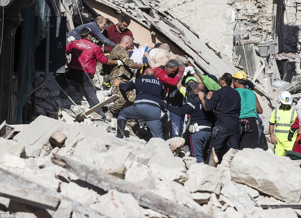 Escapar: Um homem ferido coberto de pó é feita de um edifício em ruínas em uma maca por uma equipe de trabalhadores de resgate em Amatrice