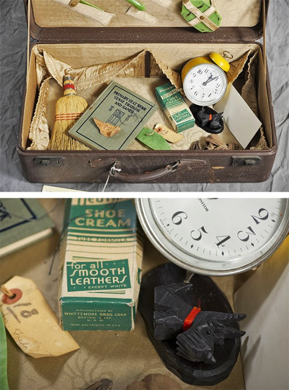 Abandoned suitcase with yellow alarm clock, straw broom, small Scotty dog figure, shoe polish cream and booklet.