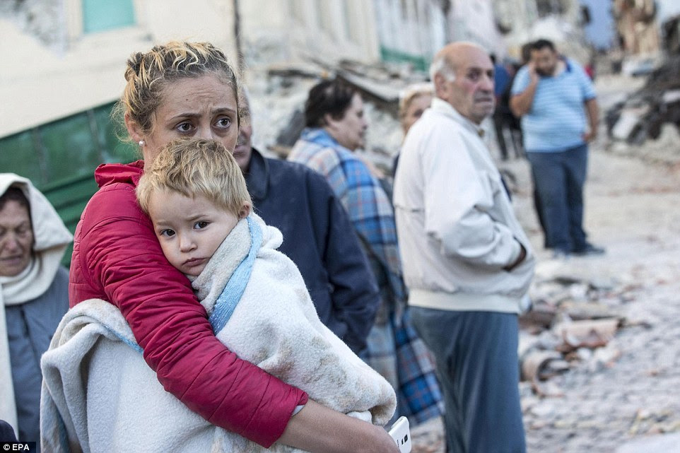 Uma mãe abraça seu filho aterrorizado em um cobertor em Amatrice como eles estão ao lado de outros moradores da cidade