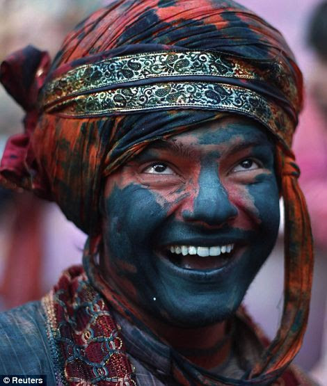 A man daubed in coloured powder smiles as he celebrates Lathmar Holi