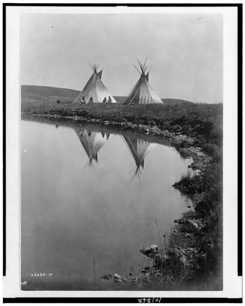 Description of  Title: At the water's edge--Piegan.  <br />Date Created/Published: 1910, c1910.  <br />Summary: Two tepees reflected in water of pond, with four Piegan Indians seated in front of one tepee.  <br />Photograph by Edward S. Curtis, Curtis (Edward S.) Collection, Library of Congress Prints and Photographs Division Washington, D.C.
