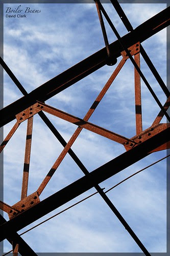 A semi-abstract composition of sky with rusty beams in a geometric arrangement.