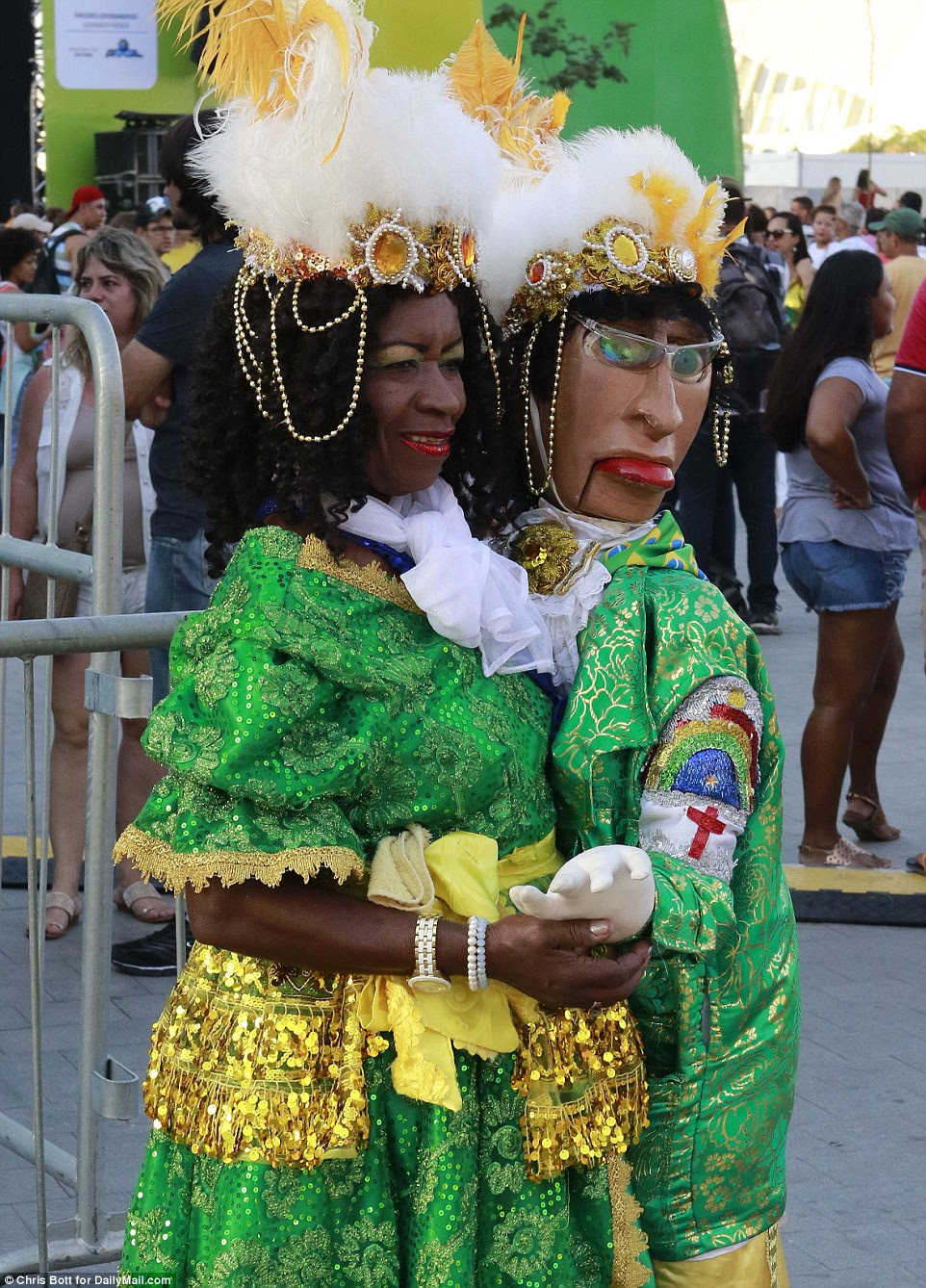 Uma mulher, em um traje verde e dourado elaborado, realizou um manequim com roupas combinando, enquanto esperava para a cerimônia