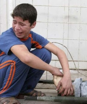 Iraqi boy at a morgue, holding the feet of his dead father