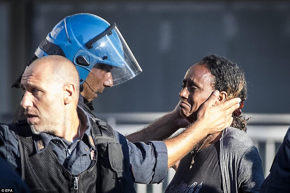 The refugees stood defiant in the face of the police's powerful water cannon as they were cleared from a piazza near Termini station. Pictured: A policeman comforts a crying refugee who was evicted from an adjacent office building