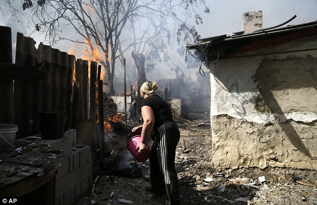 A woman throws water on her burning house in an attempt to put out the flames