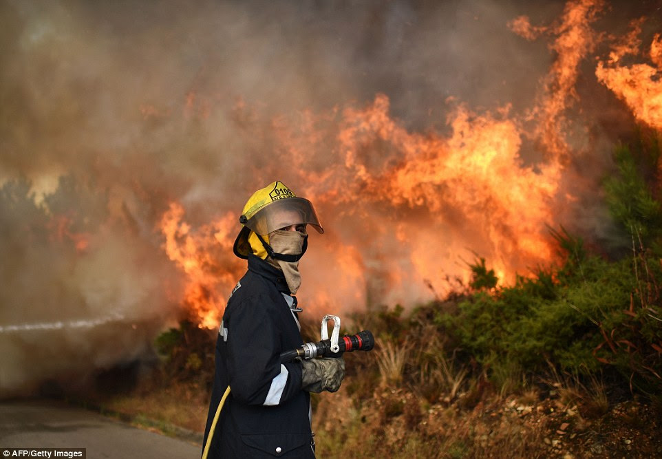 Perto deste bombeiro Português espera seu mangueira para ser conectado como um grande fogo arde fora de controle atrás dele. Houve 100 incêndios separados em Portugal continental, bem como vários na ilha da Madeira