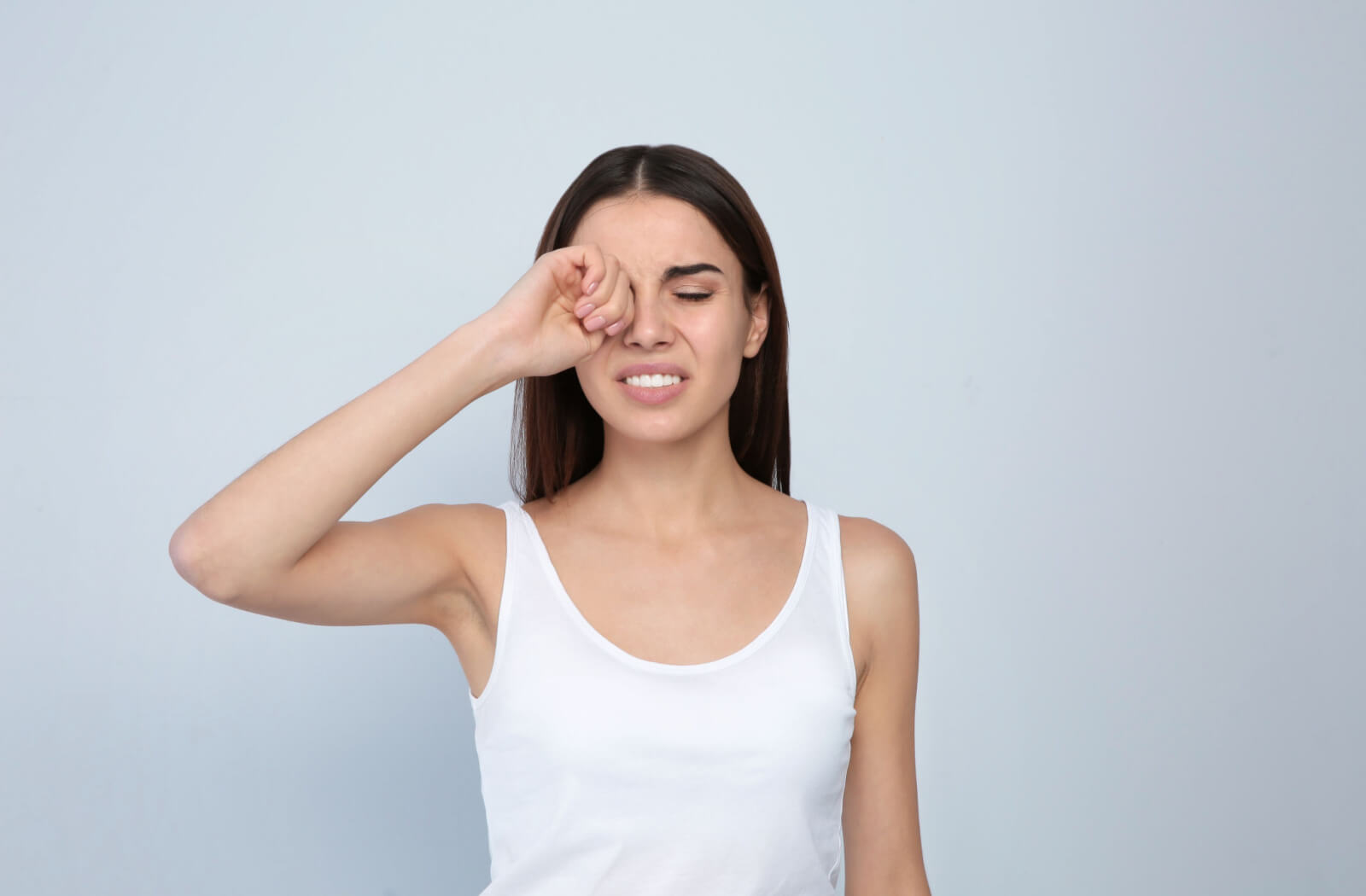 a woman rubs her eye due to grittiness caused by dry eye